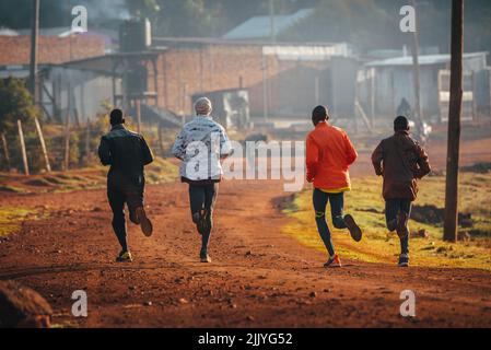 Formation de course au Kenya. Un groupe de coureurs kenyans se prépare pour un marathon et courent sur sol rouge. Course à pied, course et champ marathon. Une vie sportive simple Banque D'Images