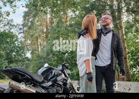 Couple d'âge moyen qui s'embrasse et s'amuse sur une moto, voyageant ensemble sur une route forestière Banque D'Images