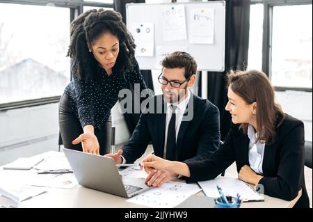 Collaboration d'équipe de professionnels. Les collègues multiraciaux qui réussissent font des brainstorming sur la stratégie ensemble, assis dans un bureau créatif moderne, étudiant des documents, utilisant un ordinateur portable, discutant Banque D'Images
