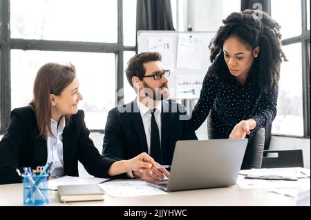 Les collègues multiraciaux font des brainstorming sur la stratégie ensemble, assis dans un bureau créatif moderne, étudiant des documents, utilisant un ordinateur portable, discutant. Collaboration d'équipe de professionnels Banque D'Images