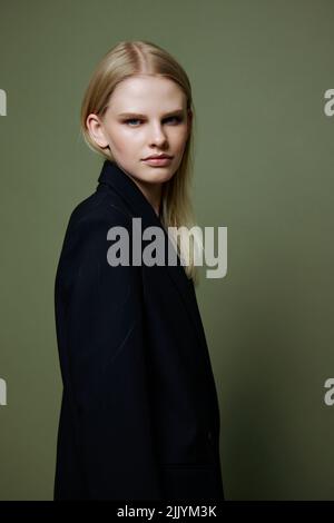 Le jeune modèle tourne et regarde la caméra par-dessus son épaule. Une offre de bannière sympa. Une fille pose en isolement dans un costume dans un studio avec un vert Banque D'Images