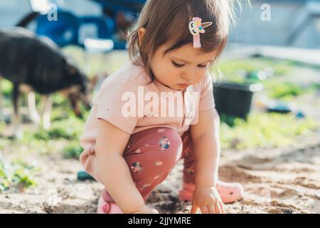 Bébé fille jouant dans le sable dans la cour de la maison explorant curieusement ce qui est dans le jardin. Tout-petit jouant avec des moules à sable. Créativité en extérieur Banque D'Images