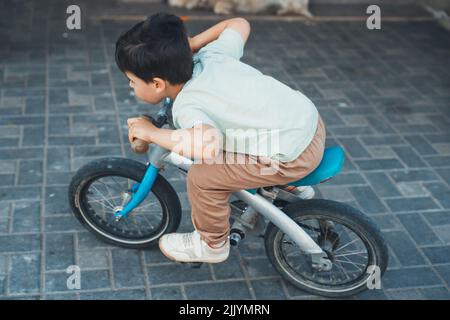 Un garçon caucasien jouant avec son vélo dans la cour de sa maison. Un garçon qui se promener rapidement dans une maison privée. Jeux pour enfants et sports de cyclisme. Banque D'Images