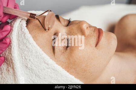 Client avec ses yeux fermés recevant un massage du visage avec un rouleau de jade dans le salon de spa. Cabinet de massage dans la clinique de beauté professionnelle. Fille Banque D'Images