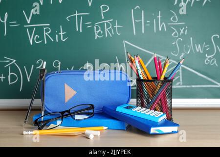 Trousse à crayons avec articles de papeterie et lunettes sur la table près du tableau noir Banque D'Images