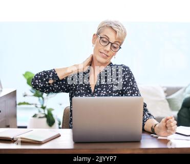 Peut-être est-il temps de faire une pause. Une femme mûre assise et souffrant d'une douleur au cou tout en utilisant son ordinateur portable pour travailler de la maison. Banque D'Images