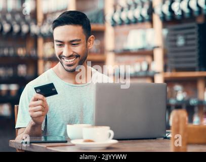 Homme faisant des achats en ligne, l'achat ou le prêt avec carte de crédit et ordinateur portable dans un café Internet. Un jeune homme heureux qui paye une dette d'assurance sur un numérique Banque D'Images