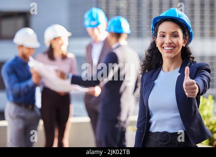 Vous ne regretterez pas votre décision : une jeune femme d'affaires se tenant dans la ville et montrant un geste de pouce tout en portant un casque. Banque D'Images