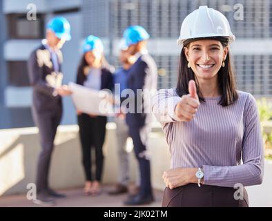 Vous allez adorer votre nouveau bâtiment. Une jeune femme d'affaires se tenant dans la ville et montrant un geste de pouce tout en portant un casque. Banque D'Images