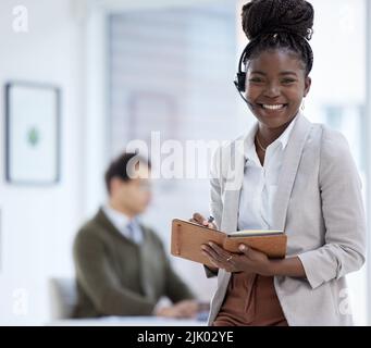 Rester organisé et à la pointe de la situation. Portrait d'une jeune femme d'affaires portant un casque et écrivant des notes tout en travaillant dans un bureau. Banque D'Images