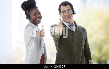 Nous garantissons le meilleur en matière de service à la clientèle. Portrait de deux agents de centre d'appels montrant les pouces dans un bureau. Banque D'Images
