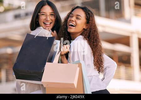 Gagnez des dollars pour dépenser des dollars. Deux jeunes femmes attrayantes debout à l'extérieur et se liant tout en faisant du shopping dans la ville. Banque D'Images