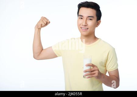 Portrait à la taille du beau asiatique qui fléchit les muscles tout en tenant un verre de lait à la main, isolé sur fond blanc Banque D'Images