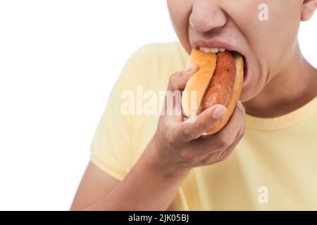 Gros plan d'un jeune homme méconnaissable qui mord un délicieux hot dog sur fond blanc Banque D'Images