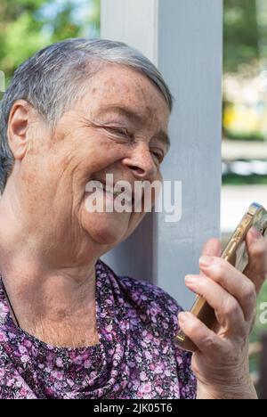 femme âgée avec téléphone intelligent ayant des appels vidéo le jour ensoleillé dans le parc. Portrait en gros plan de la femme sénitrice qui parle lors d'un appel vidéo mobile, heureux Banque D'Images