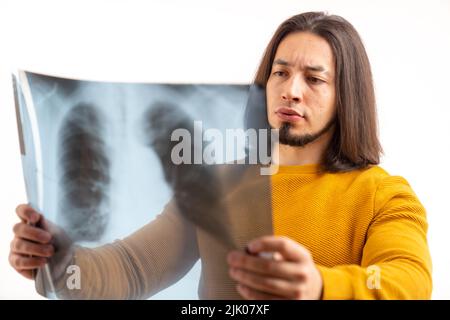 Jeune homme hispanique isolé, à poil long, suspendu et analysant une photo à rayons X de sa poitrine. Photo de haute qualité Banque D'Images