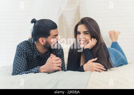 Jeune couple blanc se relaxant dans la chambre ensemble. Petit ami regardant sa petite amie qui regarde l'appareil photo avec un grand sourire. Prise de vue en intérieur. Photo de haute qualité Banque D'Images