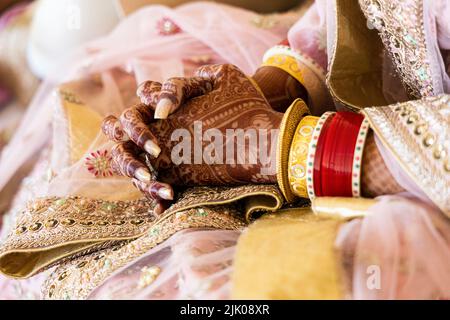 Belle mariée indienne portant des bracelets rouges et des bijoux en or. Motif Mehndi ou Henna sur les mains. Nouvelle mariée indienne au mariage. Banque D'Images