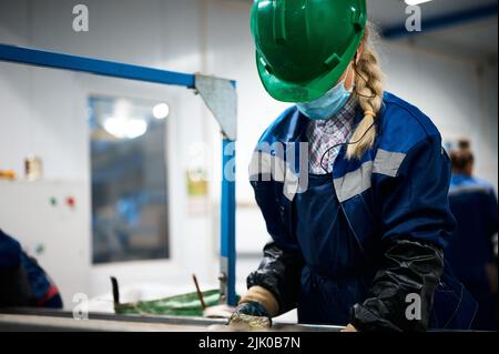 Une femme dans un casque trie les déchets à la courroie du convoyeur dans l'atelier Banque D'Images