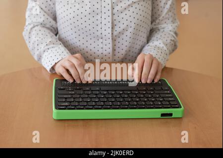 Une femme aveugle utilise un ordinateur avec un écran en braille et un clavier d'ordinateur. Périphérique inclus. Banque D'Images