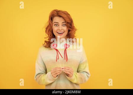 émerveillement heureux redhead femme avec coeur rouge bâtons sur fond jaune. amour Banque D'Images