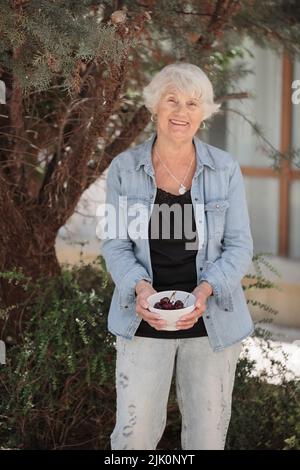 Femme âgée tenant un bol de cerises mûres Banque D'Images