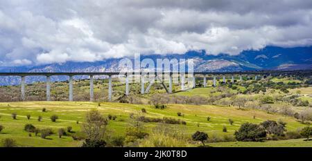 Viaduc ou pont où passe le train à grande vitesse, dans un paysage vert avec des nuages sombres de tempête. Madrid. Banque D'Images