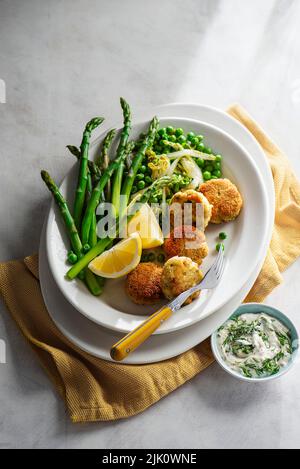 Fiscakes avec des letces et des petits pois cuits au beurre, asperges et sauce tartare Banque D'Images