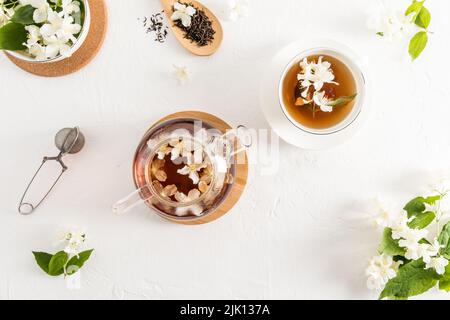 composition du thé sur fond blanc. théière en verre avec thé au jasmin, tasse de thé blanc, passoire, feuilles de thé sèches. vue du dessus Banque D'Images