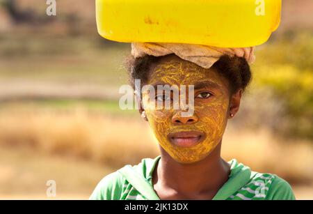 Portrait d'une femme transportant de l'eau, avec son visage peint pour protéger la peau du soleil, Isalo, Madagascar, Afrique Banque D'Images