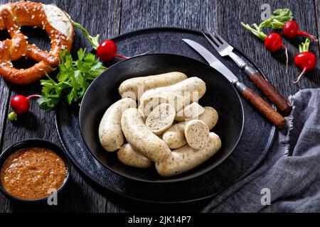 Weisswurst dans un bol noir, saucisses blanches bavaroises de veau haché, bacon de porc, épices et persil, servies avec des bretzels doux, des radis rouges frais Banque D'Images