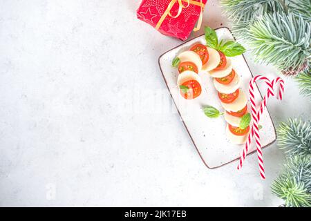 Salade Caprese de Noël en forme de Candy Cane, Mozzarella et tomates sur l'assiette servi pour le nouvel an et Noël, avec décor de Noël sur table blanche Banque D'Images