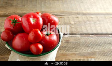 Tomates mûres rouges avec gouttes d'eau dans un bol en céramique sur fond de bois. Le concept de la cuisine végétarienne. Orientation horizontale. Mise au point sélective. Banque D'Images