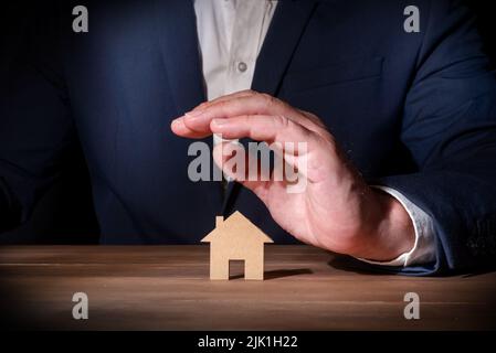 Professionnel de l'assurance couvrant une maison en carton avec sa main. Assurance habitation et incendie. Protection contre les événements imprévus à domicile Banque D'Images
