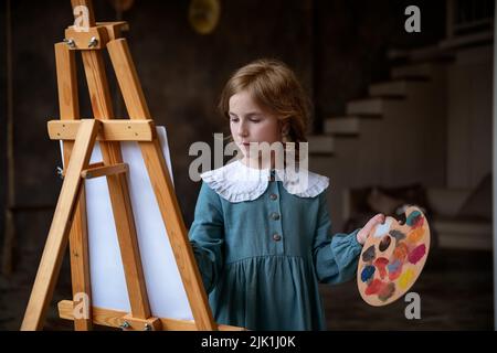 une petite fille mignonne tire derrière un chevalet. rêvant Banque D'Images