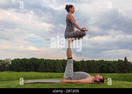 Homme allongé sur l'herbe et femme d'équilibrage dans ses pieds. Un jeune couple fait de l'acro yoga dans le parc Banque D'Images