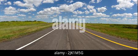 Panorama d'une route à deux voies au sommet d'une rue noire lors d'une journée ensoleillée d'été le long de l'autoroute US 94 dans le comté de Stutsman près de Medina, Dakota du Nord. Banque D'Images
