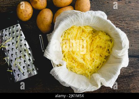 Pommes de terre Yukon Gold déchiquetées dans un saladier à doublure en tissu de fromage : vue de dessus des pommes de terre jaunes entières et déchiquetées avec une boîte de râpe Banque D'Images