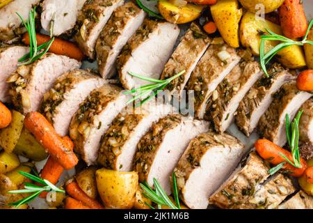 Gros plan vue de dessus de filet de porc rôti avec pommes de terre et carottes : tranches de médaillons de porc entourées de légumes sur un plateau Banque D'Images
