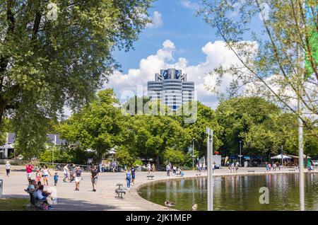 Munich, Allemagne - 6 juillet 2022 : le siège de BMW se présente sous la forme d'un moteur quatre cylindres derrière les arbres du parc olympique. Les gens marchent Banque D'Images