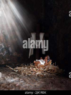 Noël. Bébé Jésus dans un mangeur, rayons de lumière le brillant avec le fond de Croix de bois. Banque D'Images