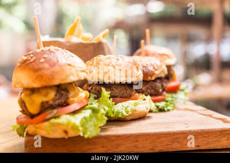 Quatre hamburgers sur une planche en bois et des frites servies dans un panier en bois dans un restaurant Banque D'Images