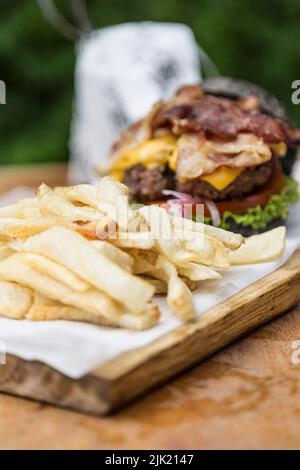 Cheeseburger avec champignons, laitue, tomate, bacon et oignons et frites sur une planche de bois Banque D'Images