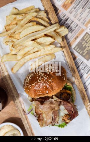 Cheeseburger avec champignons, laitue, tomate, bacon et oignons et frites sur une planche de bois Banque D'Images