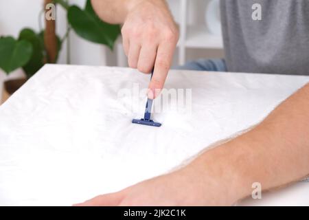Un homme enlève les pilules de tissu à l'aide d'une machine à raser jetable. Un rasoir pour enlever les granulés. Banque D'Images