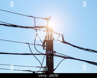 Poteau électrique en fer avec fils avec rétroéclairage solaire contre le ciel bleu Banque D'Images