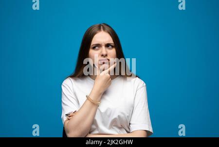 Portrait de la jeune fille bouleversée de brunette beautifil avec de longs cheveux dans un t-shirt blanc debout avec des joues bouffies isolées sur fond bleu. Émotion de Banque D'Images