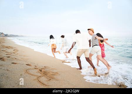 groupe de jeunes amis heureux fêtez tout en sautant et en courant sur la plage au coucher du soleil Banque D'Images