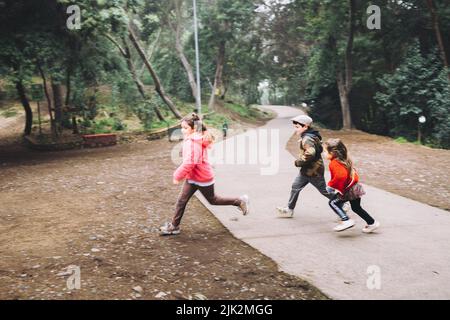 Trois enfants, une petite fille et un garçon, jouant, riant et courant sur une route de parc. Banque D'Images
