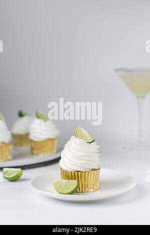 Cupcake de citron vert sur une assiette avec d'autres cupcakes en arrière-plan, cupcake de margarita avec crème blanche de beurre et un coin de lime, cupcake de margarita Banque D'Images